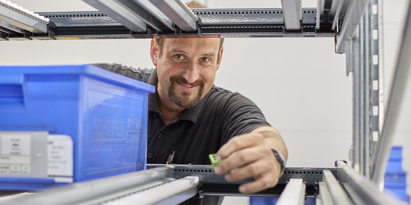 Technicien travaillant sur un équipement électrique avec un système de rayonnage et des bacs de rangement bleus
